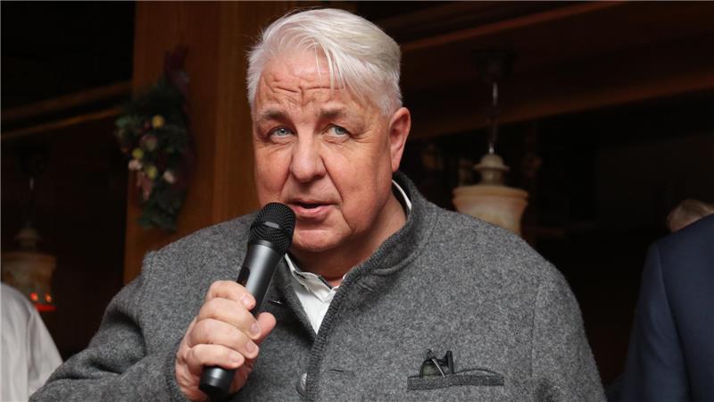 Älterer Mann mit grauem Sakko hält ein Mikrofon in der rechten Hand.