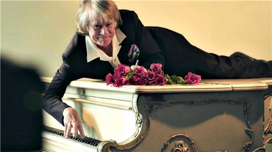 Helge Schneider liegt auf einem Klavier in einer Szene des Films „Helge Schneider - The Klimperclown“, der nun in der Mediathek zu sehen ist und am Mittwoch, 20.8., im Ersten gezeigt wird.