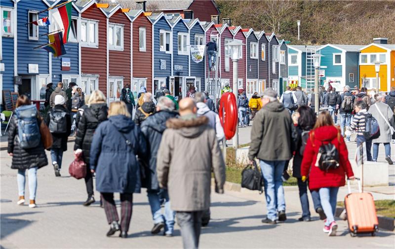 Helgoland-Besucher gehen nach ihrer Ankunft per Schiff über die Hafenstraße Richtung Inselzentrum.