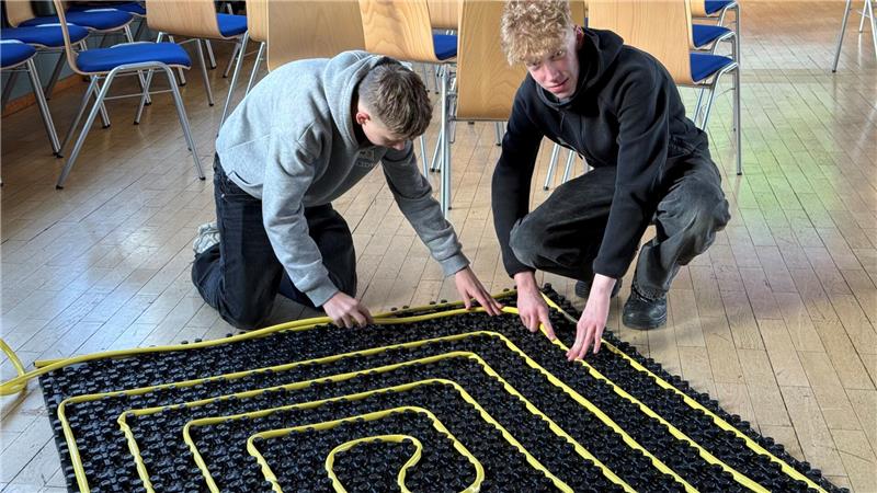 Das Foto zeigt zwei Schüler, die einen Schlauch auf einer Fläche verlegen.