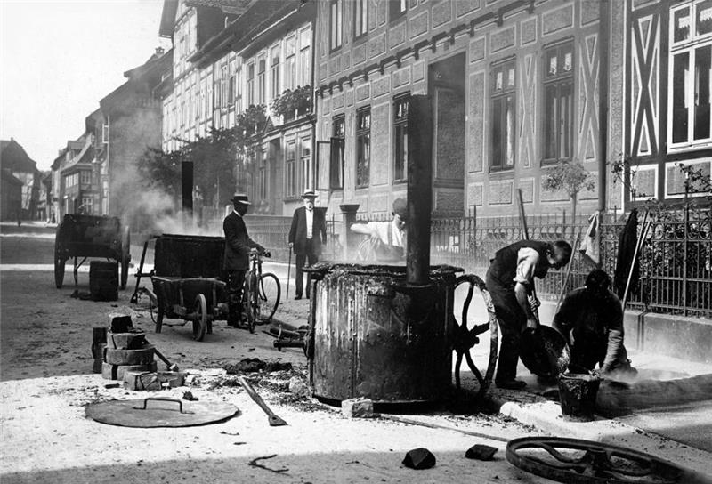 Auf der Frankenberger Straße vor mehr als hundert Jahren sind Bauarbeiter dabei, eine neue Teerschicht auf den Bürgersteig aufzubringen: Ein riesiger Teerbottich steht zur Verteilung seines dampfenden Inhalts bereit: Fast meint man, den Teer zu riechen.