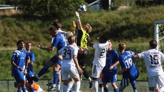 Mehrere Fußballspieler in blauen und weißen Trikots springen im Strafraum vor dem Tor um den Ball, der Torwart in gelbem Trikot hebt die Hand zum Ball hoch