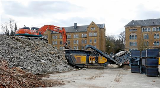 Hinten als großer Brocken hinein, vorne staubfein wieder heraus: Seit Mittwoch ist ein Steinbrecher bei den Abrissarbeiten im Pfalzquartier im Einsatz (oben). Vereinzelte Waschbeton-Reste zeigen aber noch interessante Spiegelungen (rechts). Foto: Epping