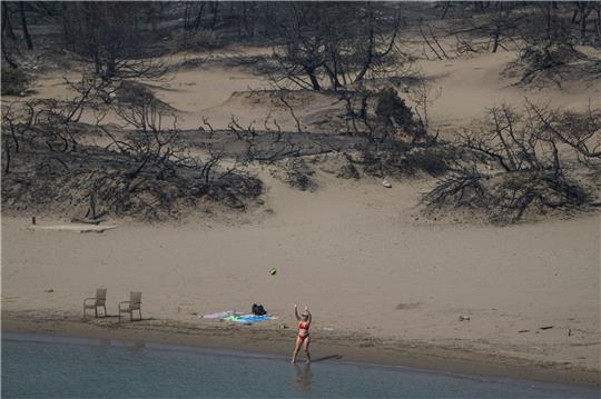 Hinten die verbrannte Vegetation, vor das Mittelmeer. Eine Frau spielt mit einem Ball am Strand bei Gennadi auf Rhodos.