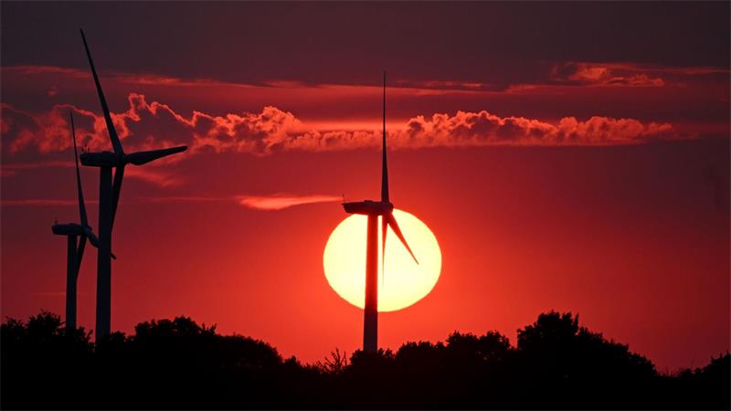 Hinter Windrädern färbt die sinkende Sonne den Himmel über Nordrhein-Westfalen rot. 