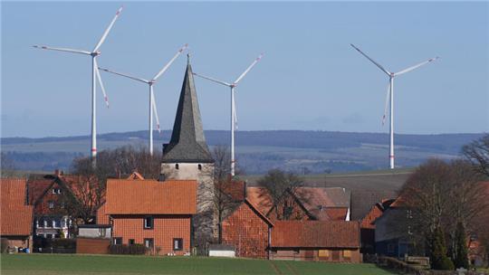 Ein Kirchturm im Vordergrund, im Hintergrund drehen sich Windkraftanlagen.