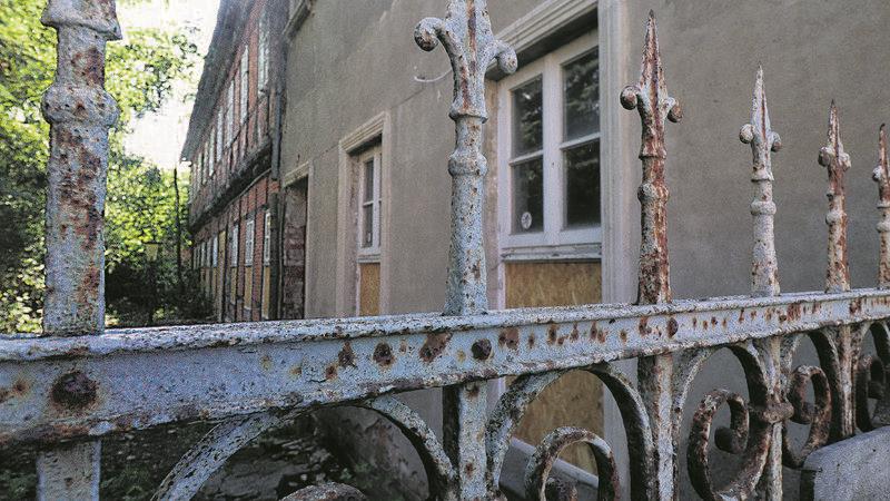 Ein vom Verfall bedrohtes Gebäude hinter einem rostenden Tor.