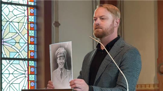 Historiker und Kirchenvorstand Frederik Kunze zeigt in seiner Ansprache ein Foto des amerikanischen Piloten und Oberleutnants John Coggeshall Saunders.