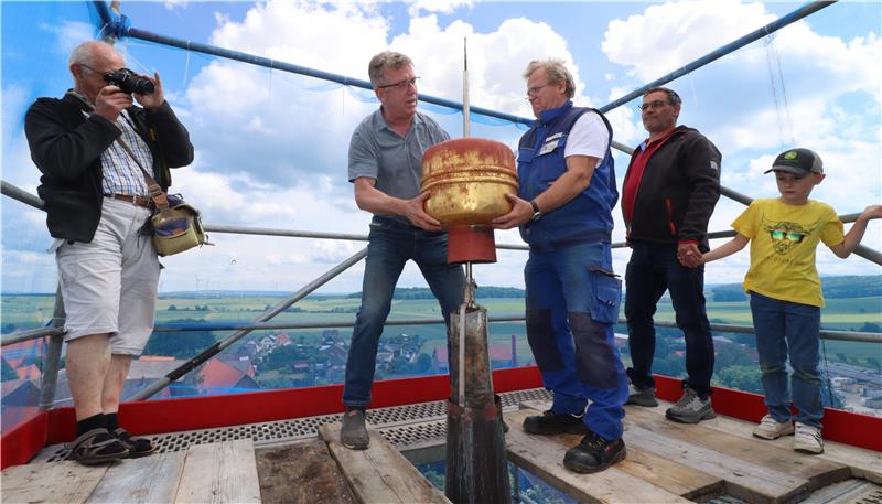 Menschen stehen auf einem Gerüst an der Kirchturmspitze, zwei Personen nehmen den Kirchturmknauf ab.