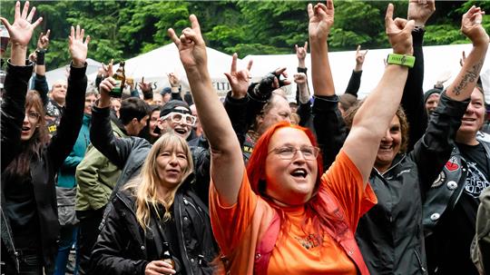 Menschen feiern beim Festival „Pfauenteiche Rocken“ in Clausthal-Zellerfeld und heben die Hände in die Luft.
