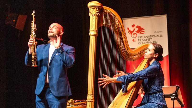 Mann im Anzug spielt Saxophon neben Frau in blauem Kleid, die Harfe spielt