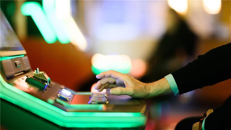 Hand einer Person, die einen Hebel an einem Spielautomaten mit grüner Beleuchtung bedient
