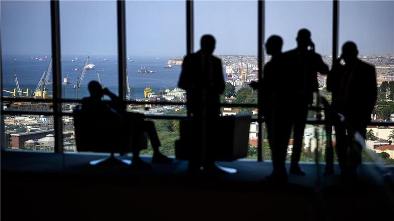 Hotelgäste stehen zum Teil telefonierend vor einem Panoramafenster in einem Luxushotel in Luanda.