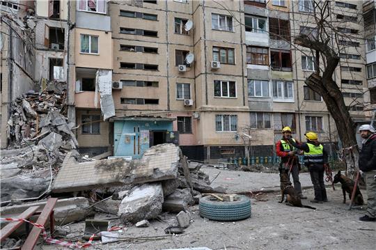 Hundeführer stehen neben einem Wohnhaus in Odessa, das von einer russischen Drohne zerstört wurde.