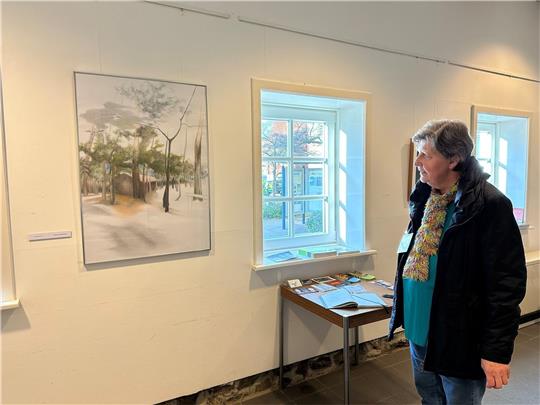 Ilona Nitsch betreut die Kunstausstellung „Natur-Mensch“ in der Rathausscheune und hat ein Lieblingsbild: Es heißt Waldhaus und ist von Claudia Schmidt. Fotos: Eggers