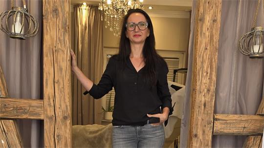 Drei Frauen in einem Raum mit Holzbalken, eine steht in der Mitte, zwei sitzen auf einer runden, mit Mosaik belegten Sitzfläche.