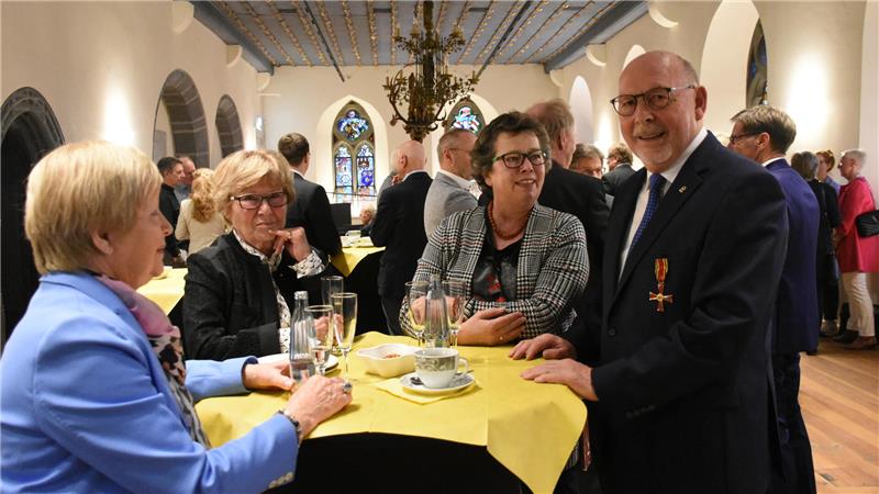 Bundesverdienstorden für den Goslarer Eike Hulsch Einige Menschen stehen in einem mit Menschen gefüllten Raum um einen Stehtisch und trinken Sekt, Wasser und Kaffee.