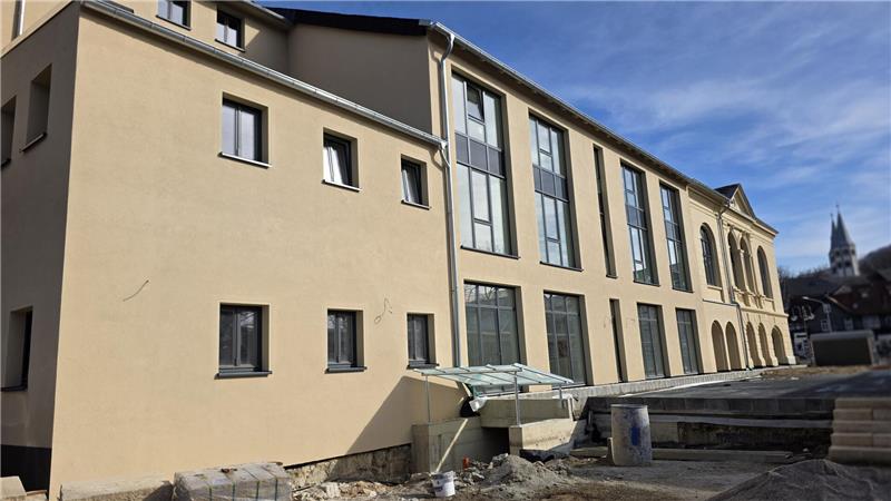 Fassade eines mehrstöckigen Gebäudes mit mehreren Fenstern und einem Glasvordach über dem Eingang bei klarem Himmel