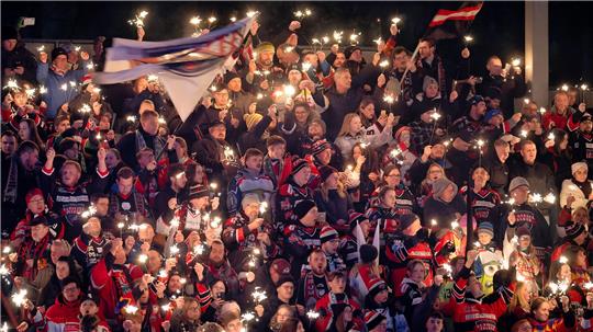 Große Menschenmenge in Sporttrikots hält Wunderkerzen und schwenkt Fahnen bei einer Veranstaltung.