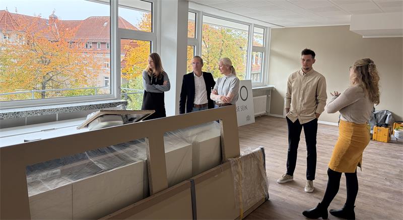 Das Foto zeigt fünf Menschen in einem leeren Raum mit verpackten Möbelstücken.