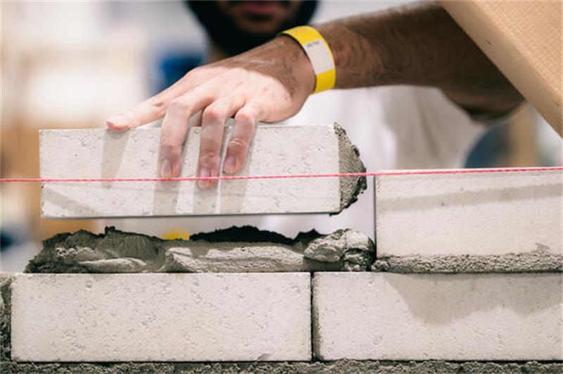 Das Bild zeigt die Hand eines Maurers, der eine Mauer oder Wand hochzieht.