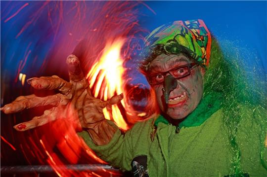 Im Hexenkostüm steht ein Besucher des Walpurgisfestes in Schierke am Feuer.