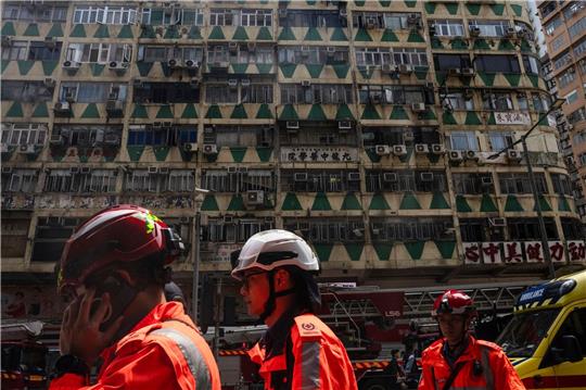 Im Hintergrund ist das ausgebrannte Hochhaus in Hongkong zu sehen - bei der Feuerwehr waren zahlreiche Hilferufe eingegangen.