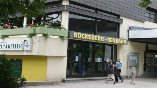 Eingang eines Gebäudes mit dem Schriftzug 'BOCKSBERG-SEILBAHN' über der Tür und drei Personen, die darauf zugehen