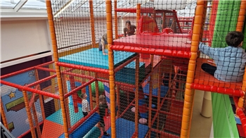 Mehrstöckige Kletteranlage mit Netzumzäunung und buntem Bodenbelag in einem Innenraum mit Kindern, die klettern und spielen.