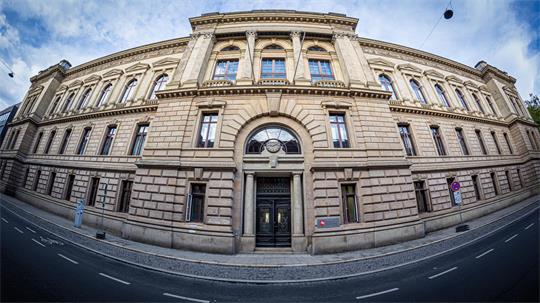 Breit aufgenommene Fassade eines historischen mehrstöckigen Gebäudes mit Säulen und verzierten Fenstern