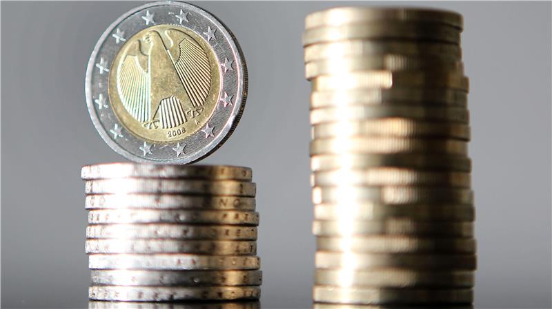 Ein Stapel Münzen mit einer 2-Euro-Münze obenauf neben einem höheren Stapel Münzen