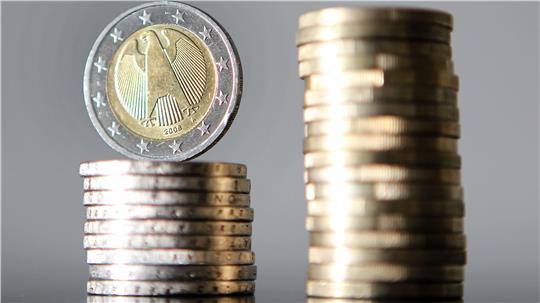 Ein Stapel Münzen mit einer 2-Euro-Münze obenauf neben einem höheren Stapel Münzen