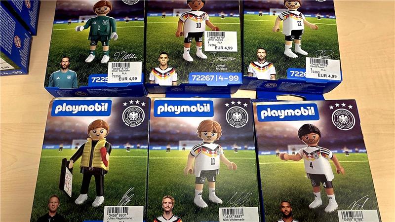 Sechs Playmobil-Figuren in Fußballtrikots der deutschen Nationalmannschaft auf Verpackungen, jeweils mit Spielerabbildung und Preisetikett.