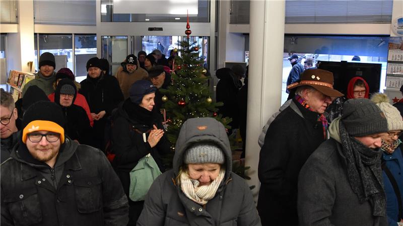 Der GZ-Schweinchenverkauf läuft in Goslar auf Hochtouren Mehrere Personen in Winterkleidung stehen in einem Innenraum mit einem geschmückten Weihnachtsbaum in der Mitte