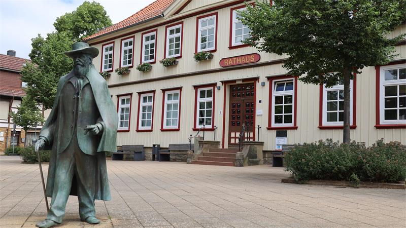 Bronzestatue eines Mannes mit Hut und Mantel vor einem Fachwerkgebäude mit der Aufschrift 'Rathaus'