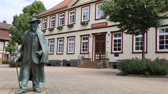 Bronzestatue eines Mannes mit Hut und Mantel vor einem Fachwerkgebäude mit der Aufschrift 'Rathaus'