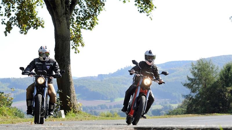 Das Bild zeigt zwei Motorradfahrer auf einer Straße mit Harzer Bergen im Hintergrund.
