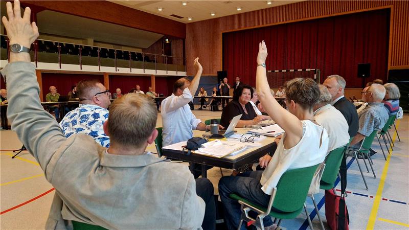 Ratsleute sitzen in der Stadthalle und manche von ihnen heben die Hand.