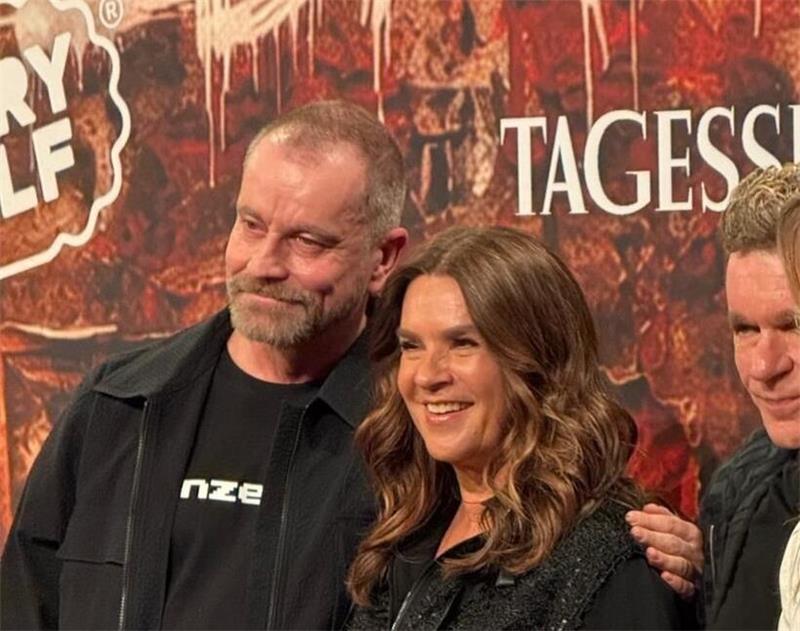 Drei Personen stehen nebeneinander vor einer Wand mit dem Schriftzug 'TAGESSPIEGEL', die mittlere Person trägt ein schwarzes, glitzerndes Oberteil,