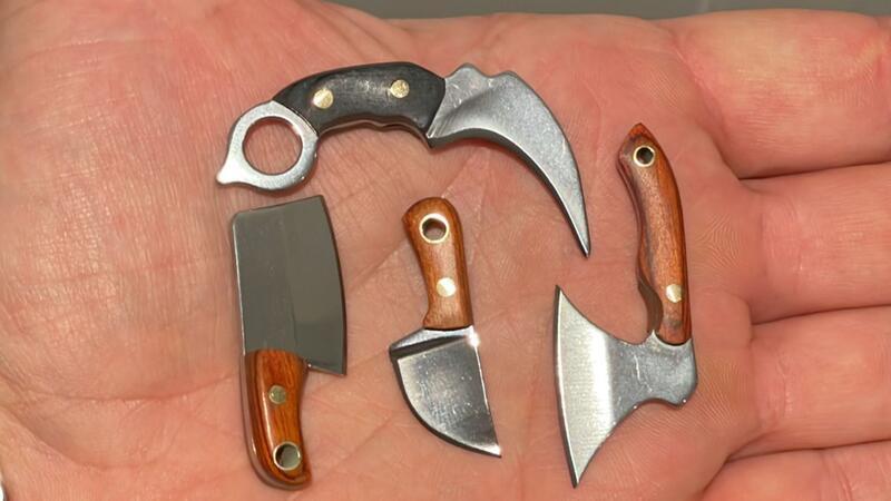 In einer Handfläche liegen vier Messer und Äxte im Miniaturformat, die nur wenige Zentimeter groß sind.