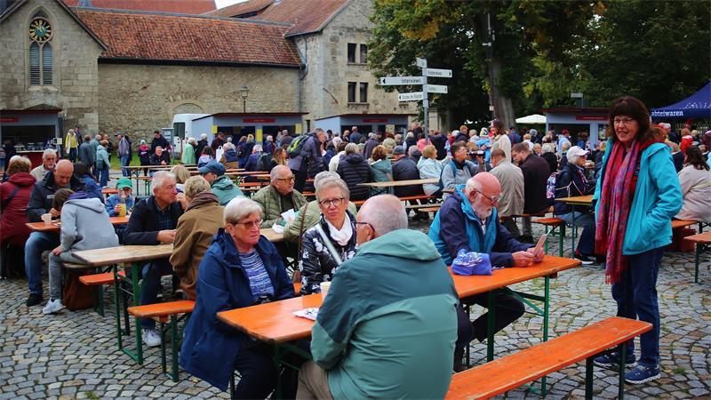 Das Foto zeigt viele Menschen die vor einem Kloster auf Bierzelt-Garnituren sitzen.
