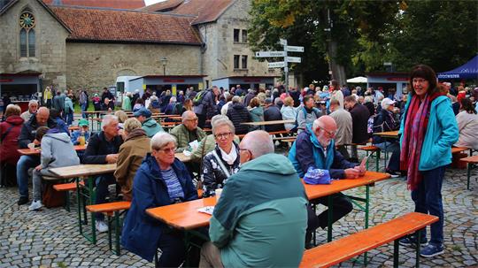 Das Foto zeigt viele Menschen die vor einem Kloster auf Bierzelt-Garnituren sitzen.