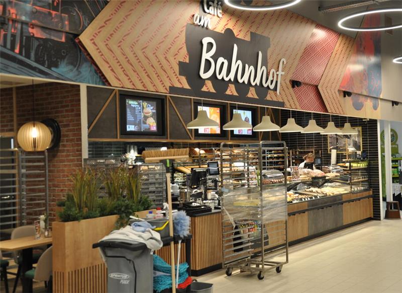 Goslarer Edeka-Center eröffnet: Erste Kunden kommen um sieben Uhr Bäckerei mit Theke, Backwaren, Beleuchtung und Reinigungswagen im Vordergrund, Schriftzug 'Bahnhof' an der Wand.