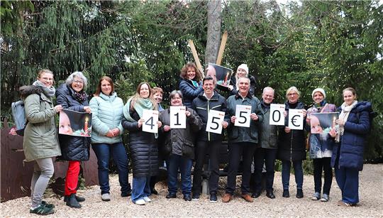 Gruppe von Menschen steht im Freien, einige halten Schilder mit den Zahlen und dem Eurozeichen '4 1 5 5 0 '.