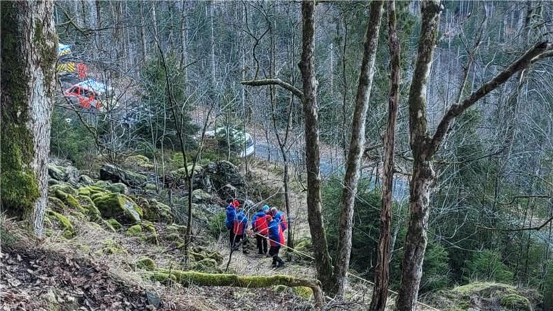 Mehrere Menschen tragen hinter Bäumen verdeckt eine verletzte Person einen Steilhang hinunter.