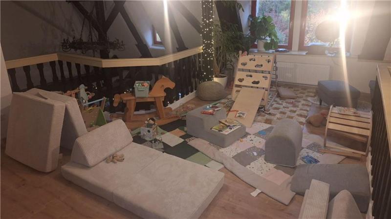 Wohnzimmer mit mehreren Sitzkissen, einem niedrigen Tisch, einer Lichterkette an der Wand und einem Fenster im Hintergrund.