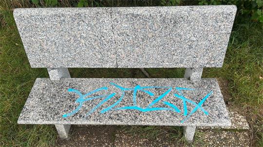 Das Bild zeigt eine Bank aus Stein, deren Sitzfläche mit Farbe beschmiert ist. 