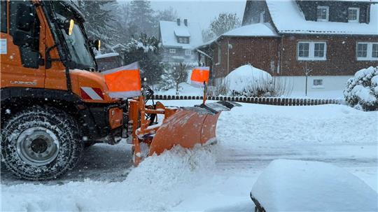 Ein Schneepflug fährt durch ein verschneites Wohngebiet.