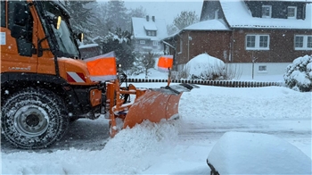 Ein Schneepflug fährt durch ein verschneites Wohngebiet.