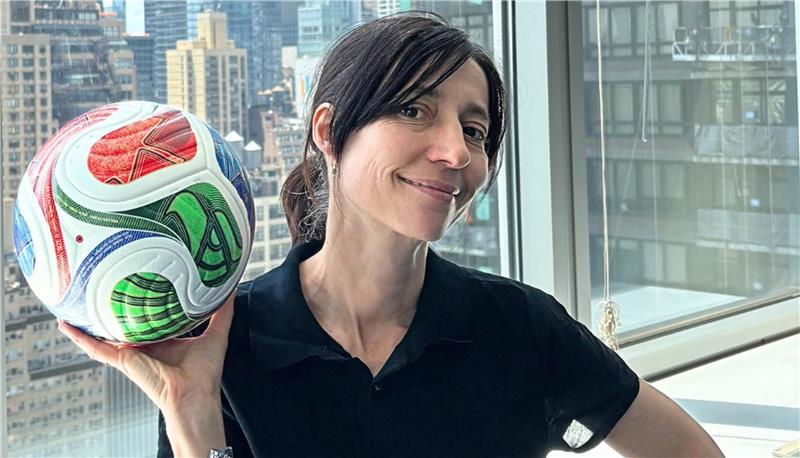 Das Foto zeigt Lisa Hollenbach vom Generalkonsulat der Bundesrepublik Deutschland in Manhattan mit einem Fußball in der rechten Hand. Aus dem Fenster hinter ihr ist die Skyline von Manhattan zu sehen.